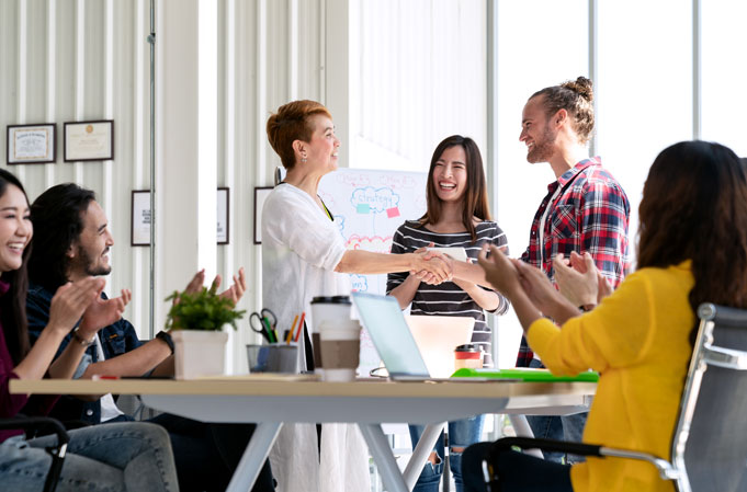 Smiling employees holding hands in front of a table of happy employees