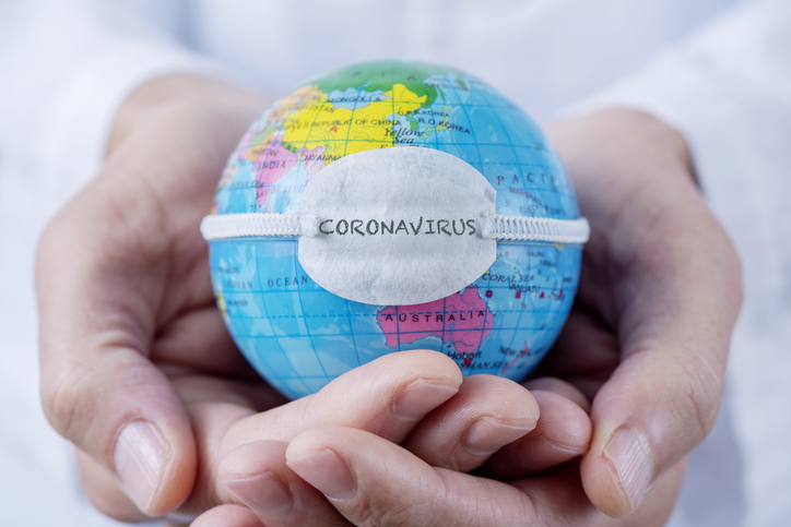 Hands holding a small globe with a mask on it. Coronavirus is written on the mask.