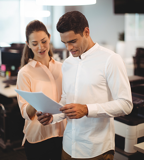 Equitable_How_Does_It_Work_Image_V1 Employee reading a paper while another employee looks on