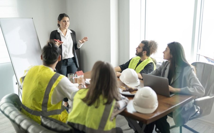 A professional teaching safety training to a table of construction workers in vests